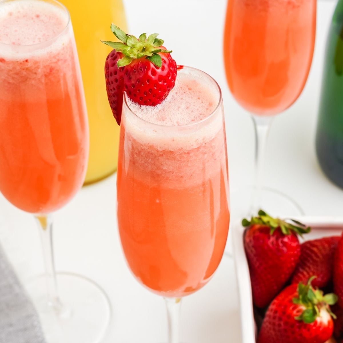 Three strawberry mimosa cocktails in champagne flutes garnished with fresh strawberries