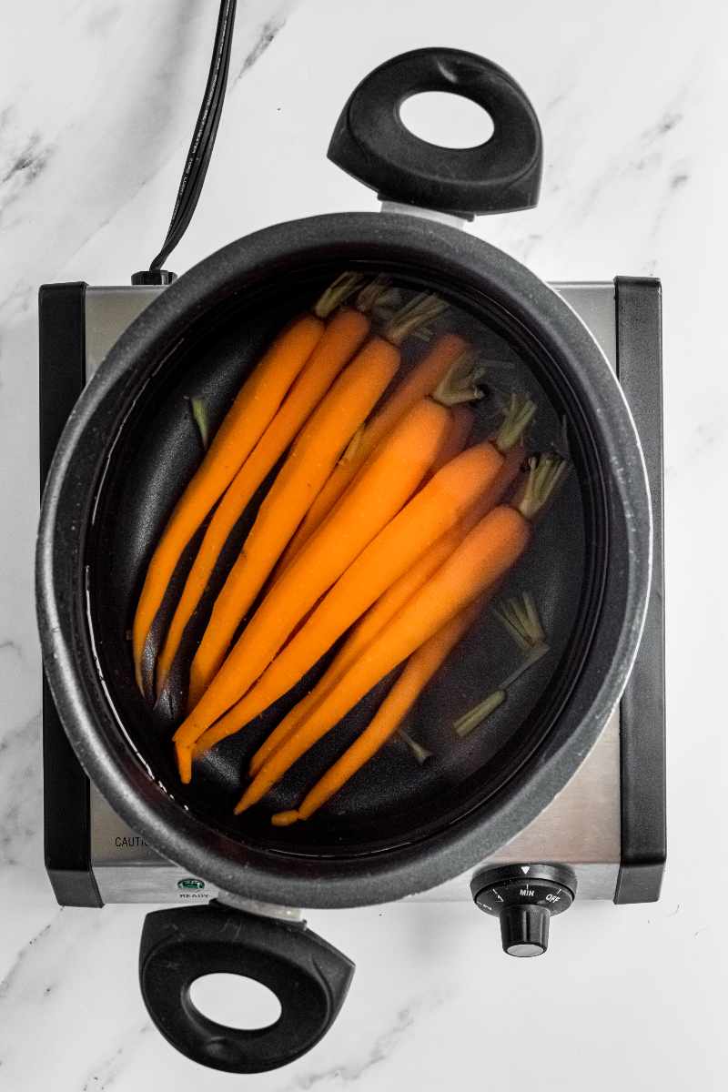 Peeled and trimmed carrots in a saucepan of water coming up to a boil.