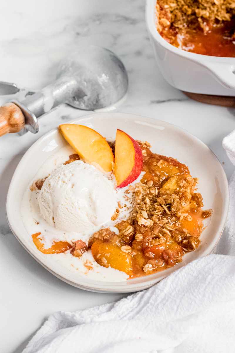 Peach crisp and a scoop of vanilla ice cream in a white bowl.