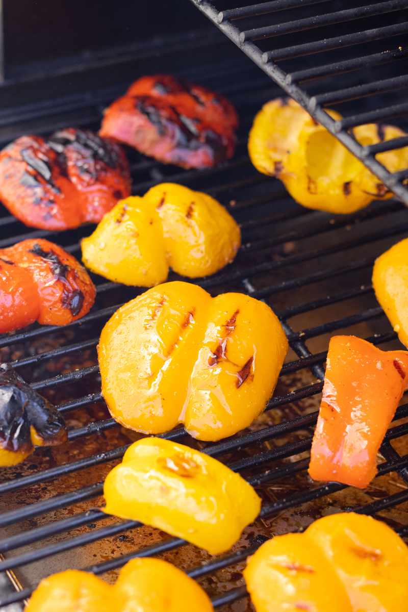 Sliced peppers grilling on gas grill grates.