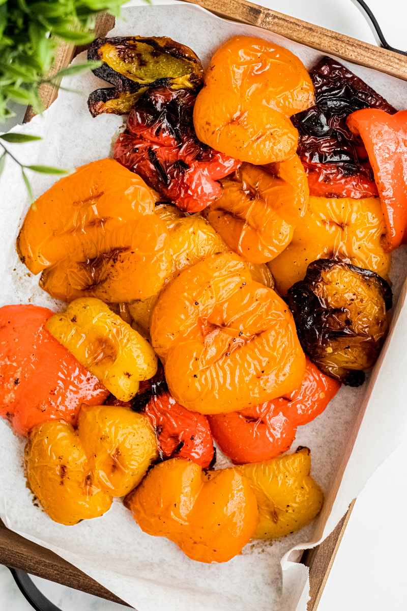 A wooden serving tray lined with parchment paper with colorful grilled bell peppers piled high.