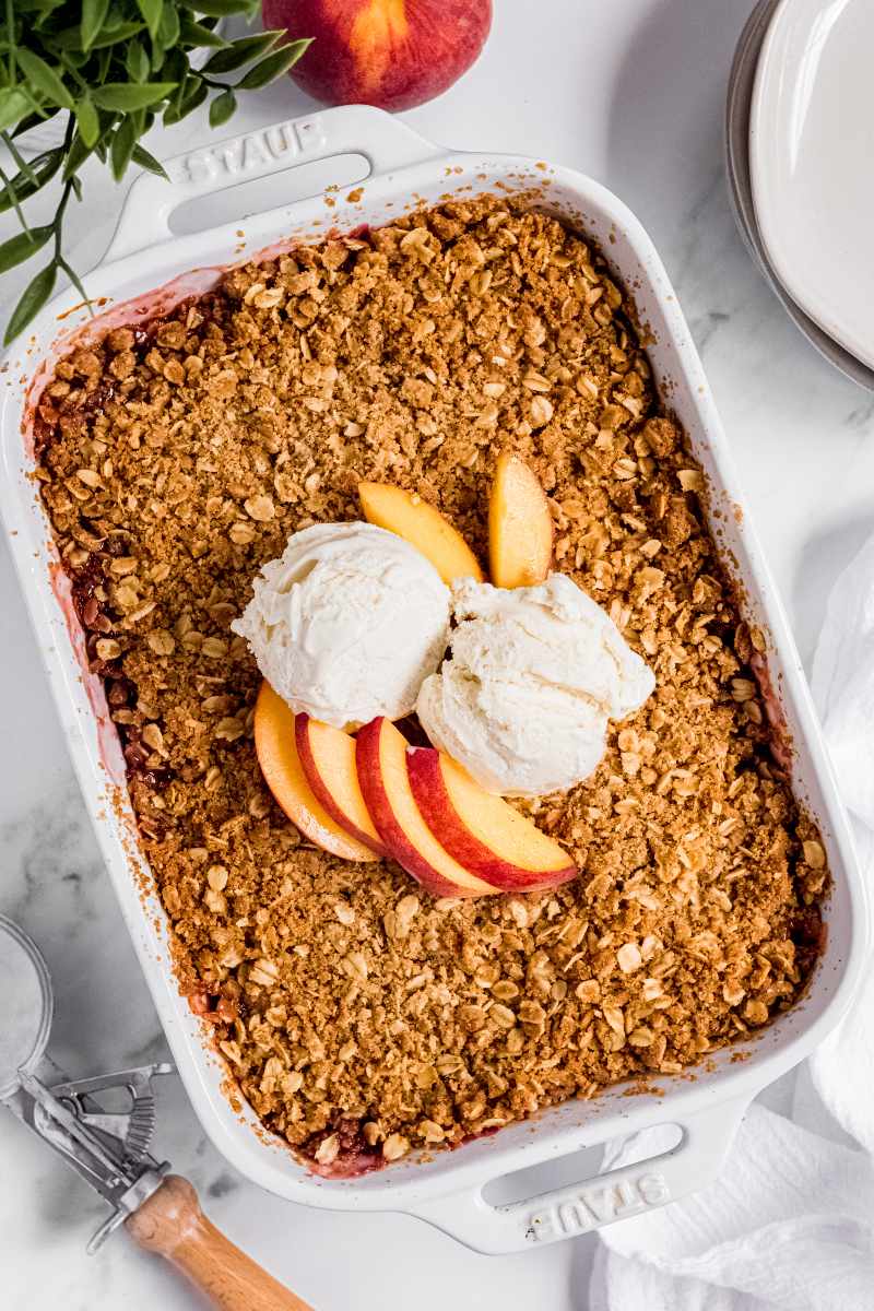 Two scoops of vanilla ice cream and some fresh peach slices on top of a finished peach crisp