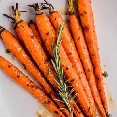 Grilled balsamic rosemary carrots on a round, white plate with a sprig of fresh rosemary on top.