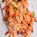 Tight view of a shrimp skewer garnished with lime zest held up above a platter of additional kabobs.