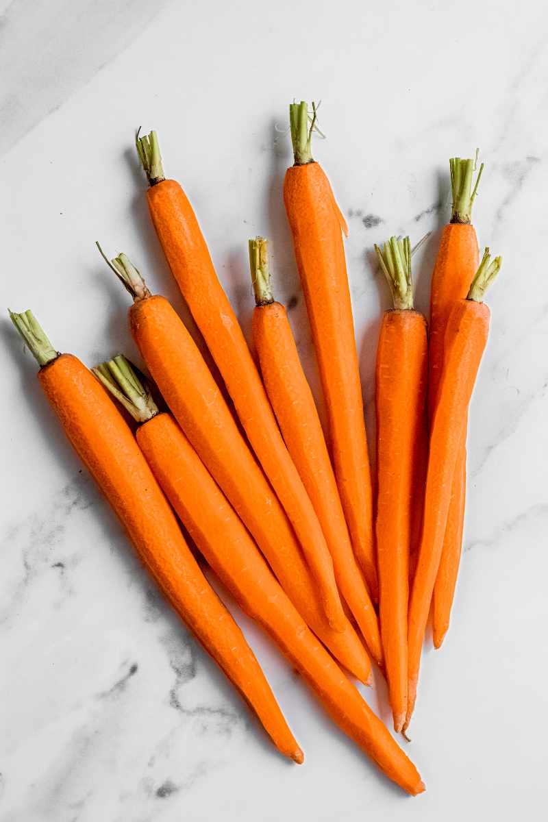 Peeled carrots with trimmed green tops in a bunch on a white marble counter.