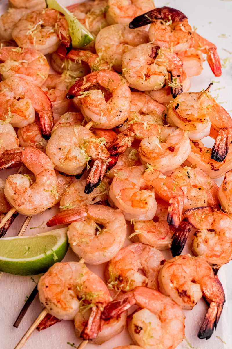 A pile of grilled coconut lime shrimp skewers with lime wedges and zest.