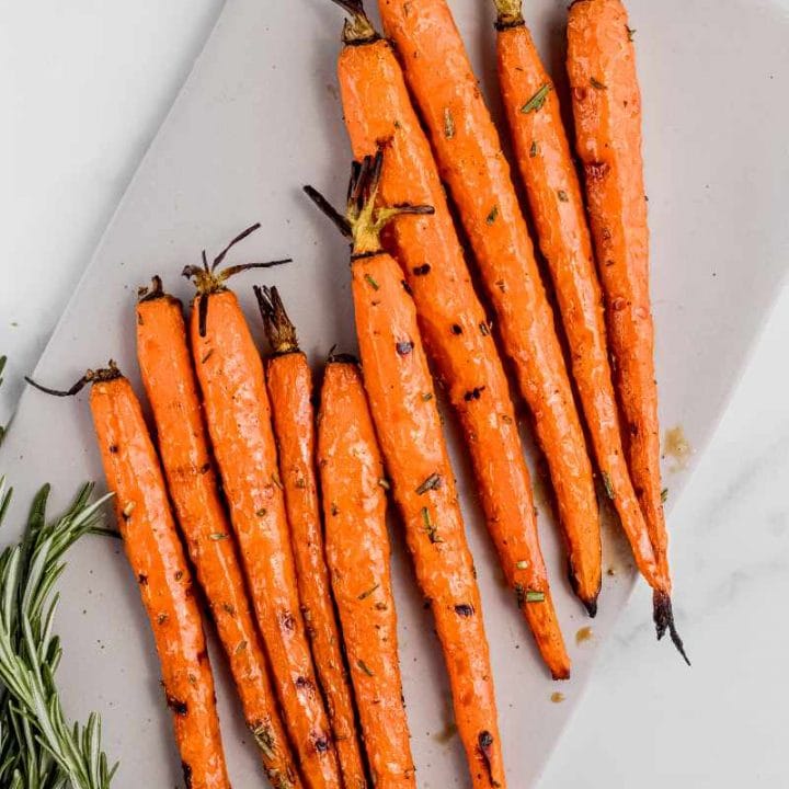 Grilled carrots arranged on a white rectangular serving platter with fresh rosemary alongside.
