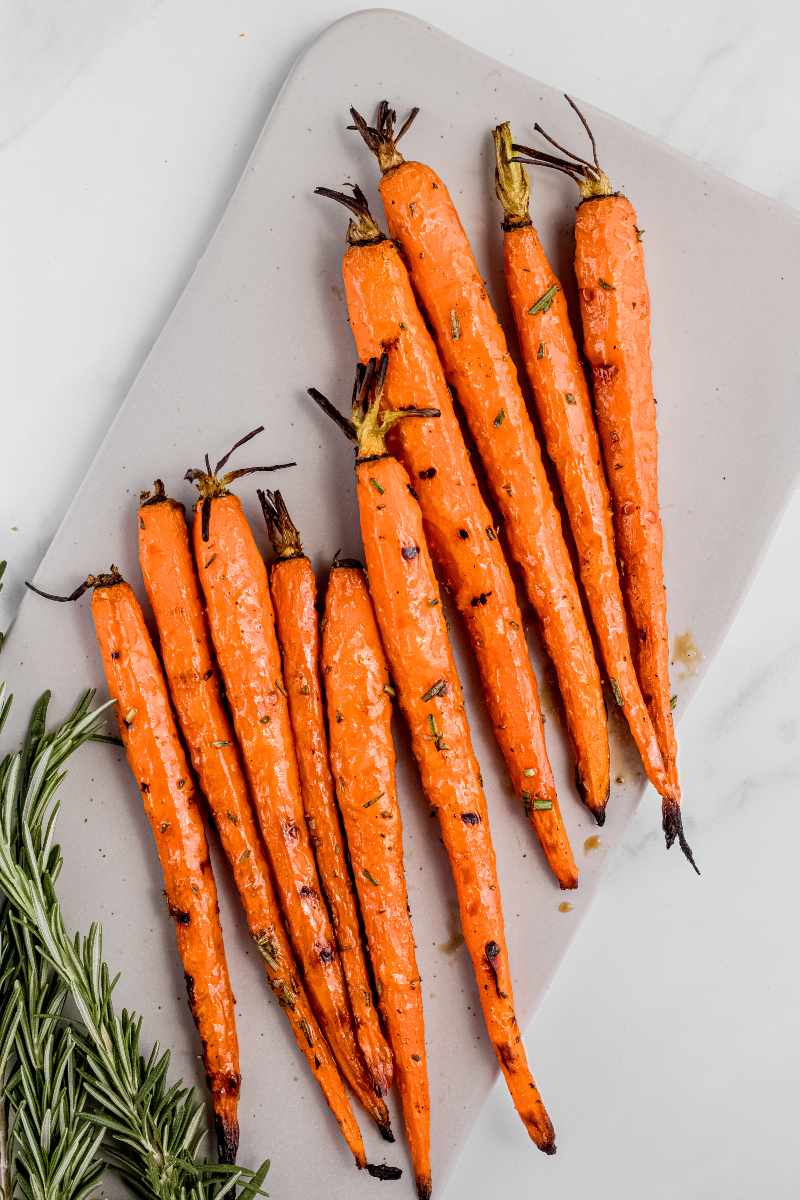 Grilled carrots arranged on a white rectangular serving platter with fresh rosemary alongside.