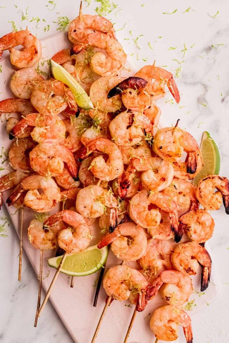 A white rectangular serving platter loaded with shrimp kabobs with lime wedges and lime zest garnish.