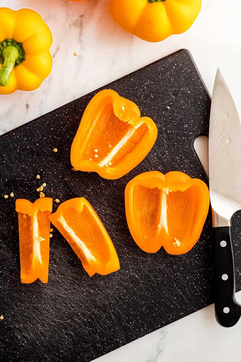 Slices of yellow bell pepper on a dark cutting board with a chef knife beside them.