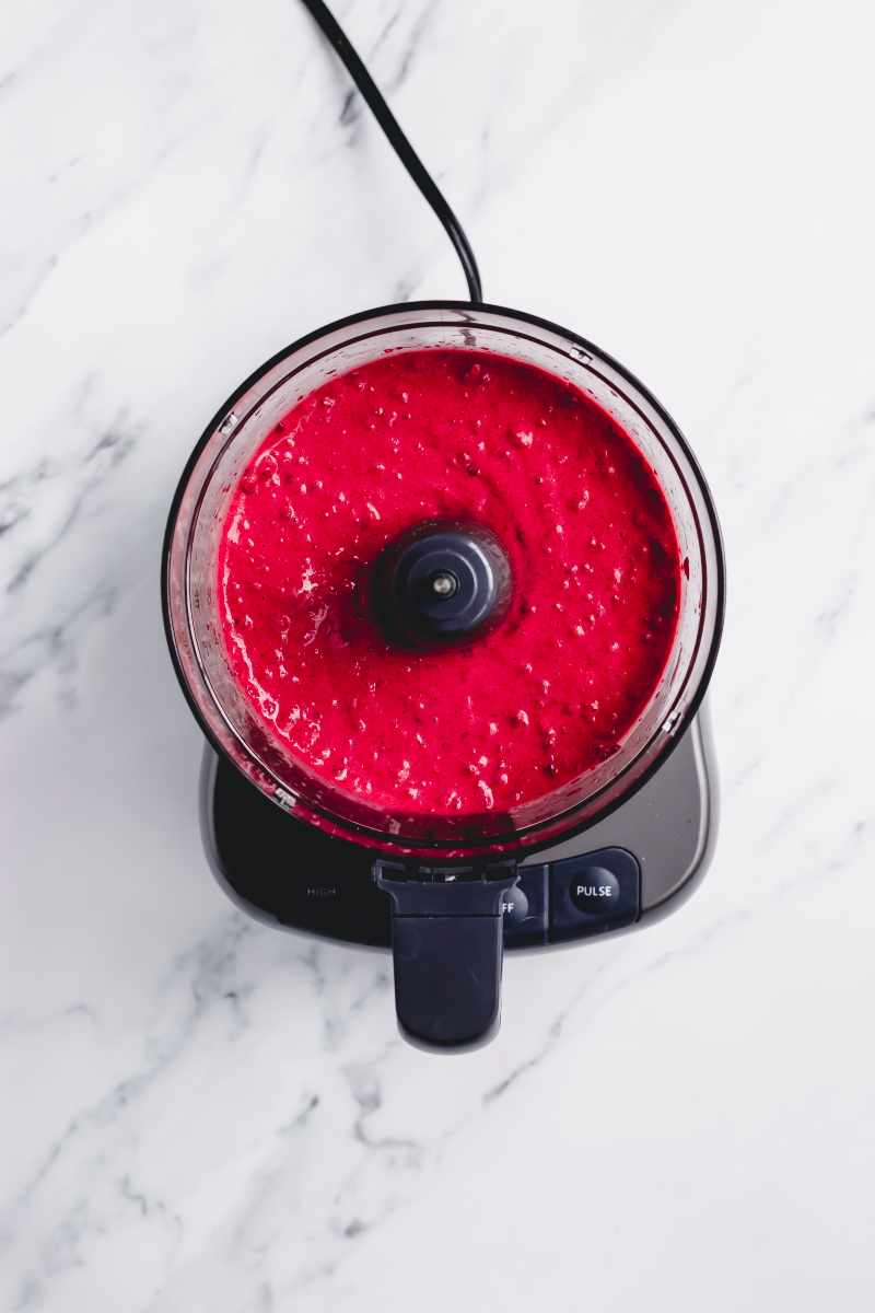 Overhead of blended raspberry mixture in the bowl of a food processor.