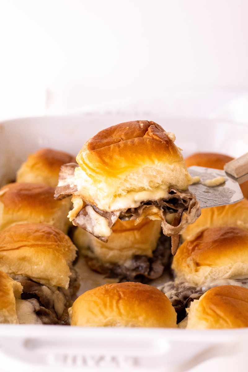 A spatula serves up an individual sandwich from a baking dish of sliders.