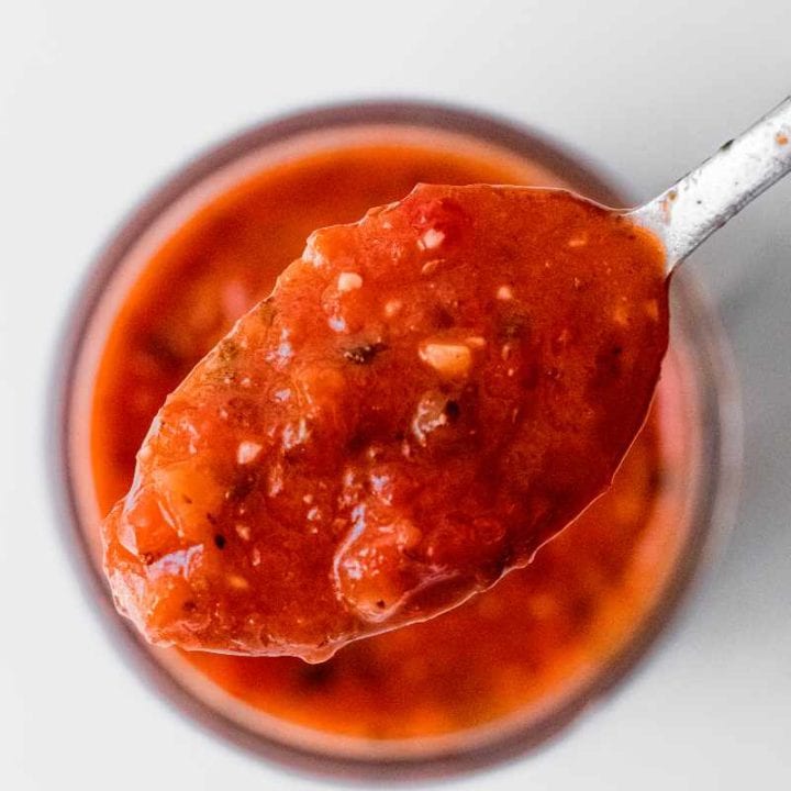 Close view of a spoonful of roasted red pepper sauce above a jar of sauce.