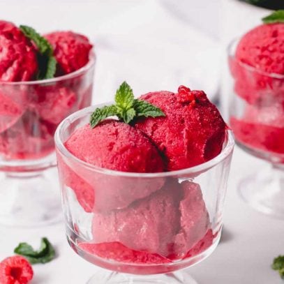 Three scoops of homemade raspberry sorbet in a bowl on a white countertop.