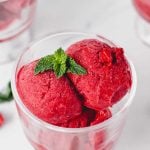 Top view of scoops of raspberry sorbet garnished with fresh mint in a footed dessert bowl.