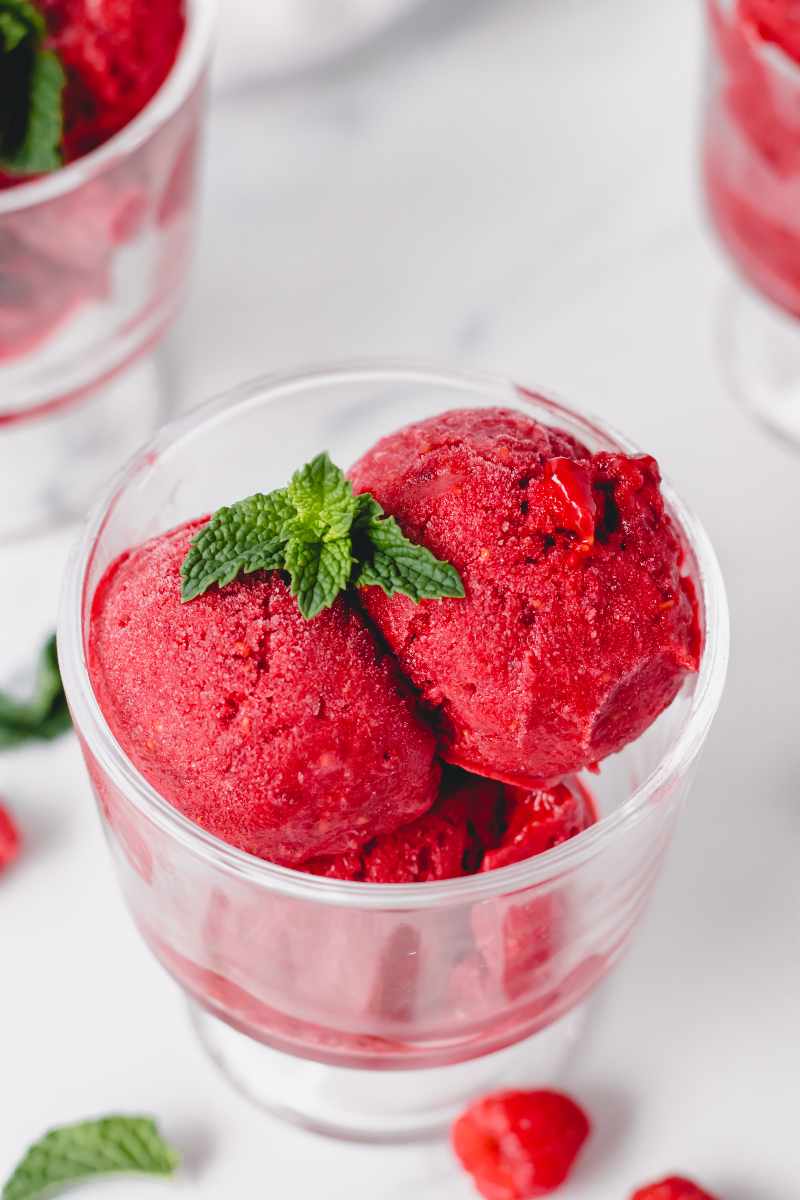 Top view of scoops of raspberry sorbet garnished with fresh mint in a footed dessert bowl.