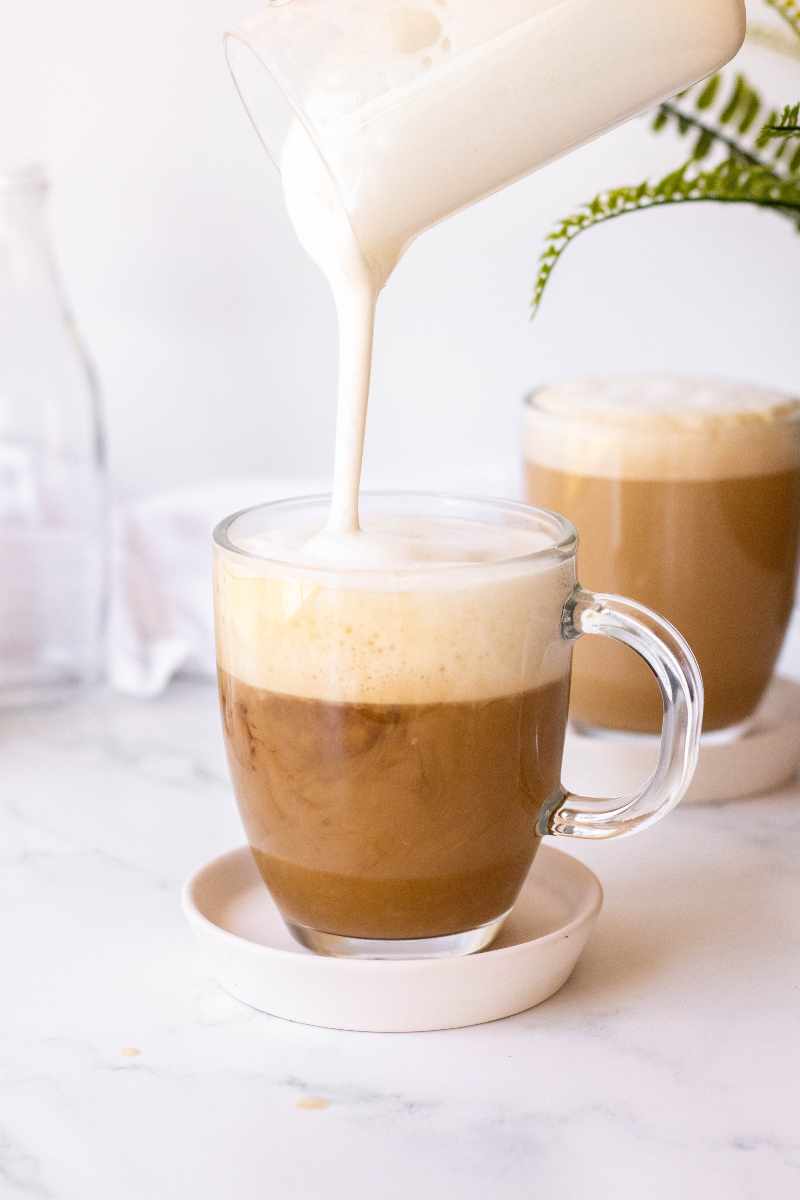Steamed milk and foam pours into a glass mug with a shot of espresso.