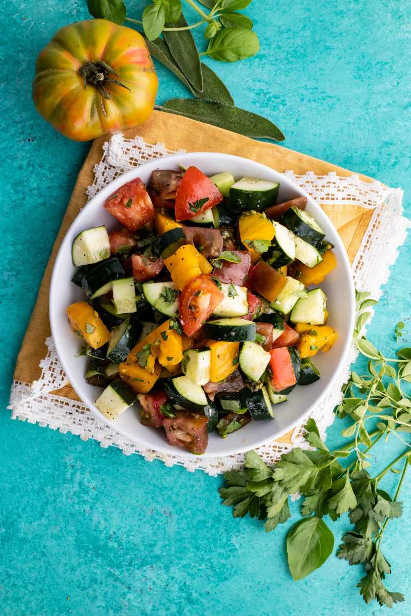 Birdseye view of a fresh herb and veggie salad in a white bowl on a blue background.