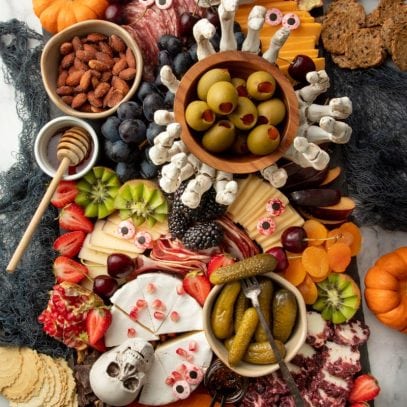 Overhead of a Halloween charcuterie board on a slate platter filled with meats, cheeses, fruits, nuts, crackers and spooky decorations.
