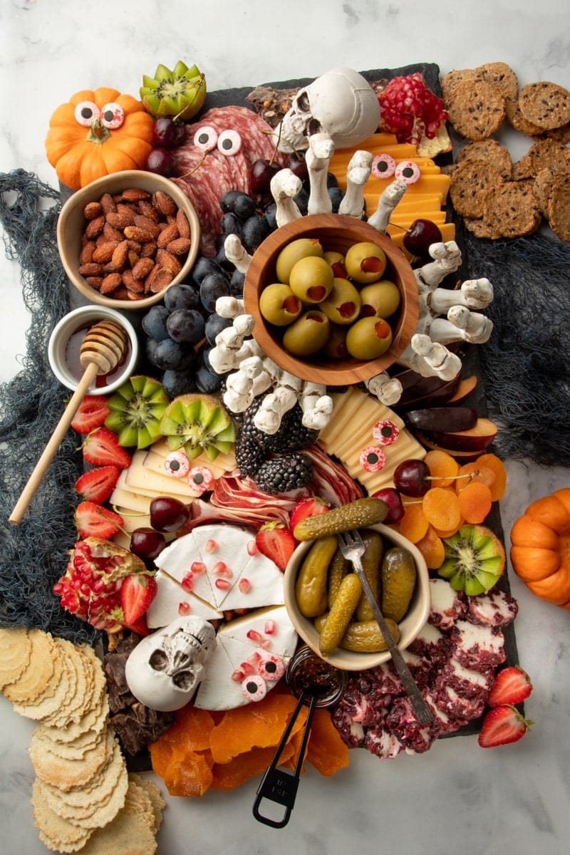 Overhead of a Halloween charcuterie board on a slate platter filled with meats, cheeses, fruits, nuts, crackers and spooky decorations.