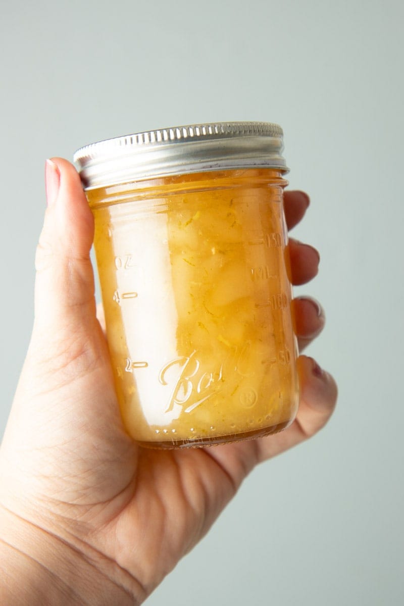 A hand holds up a half-pint jar of homemade gingered pear preserves.