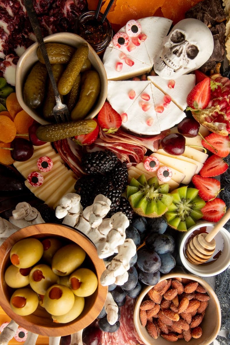 Close view of candy eyes and skeleton decorations on different cheeses surrounded by meats, fruit, and nuts.