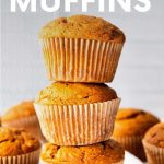 Three tender muffins stacked atop one another with cinnamon sticks and other muffins nearby. A text overlay reads, "Pumpkin Muffins."
