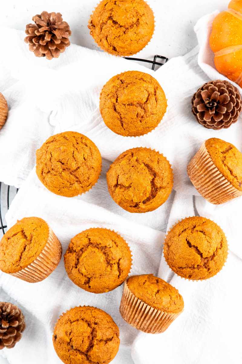 Overhead of spiced muffins resting on white kitchen linens over a black cooling rack.