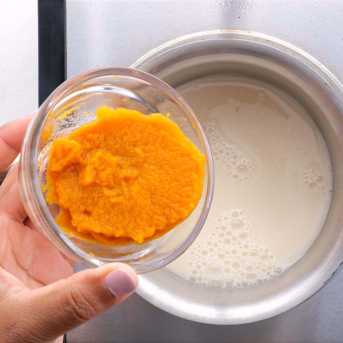 Adding pumpkin puree to milk in a saucepan to make a pumpkin spice latte