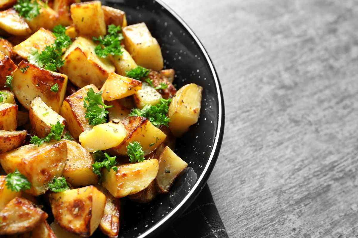 Roasted potatoes garnished with chopped fresh parsley served in a black speckled bowl.