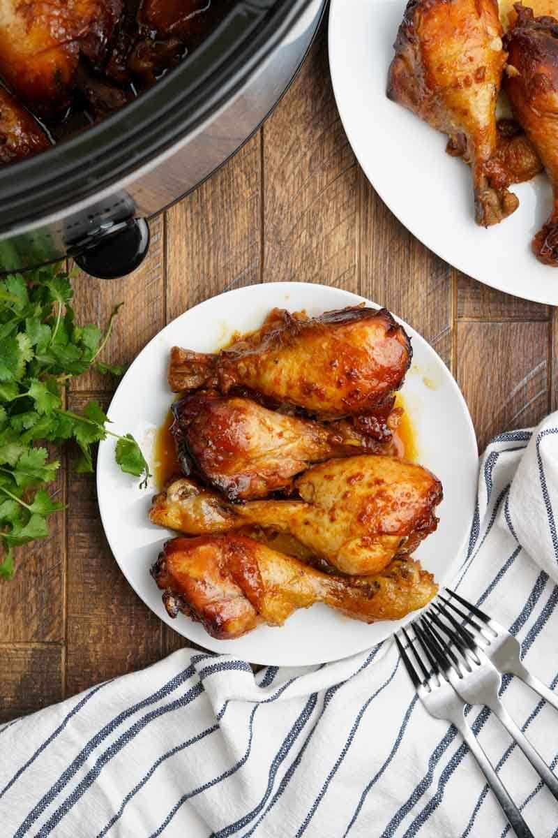 Saucy chicken drumsticks on a platter with forks nearby.