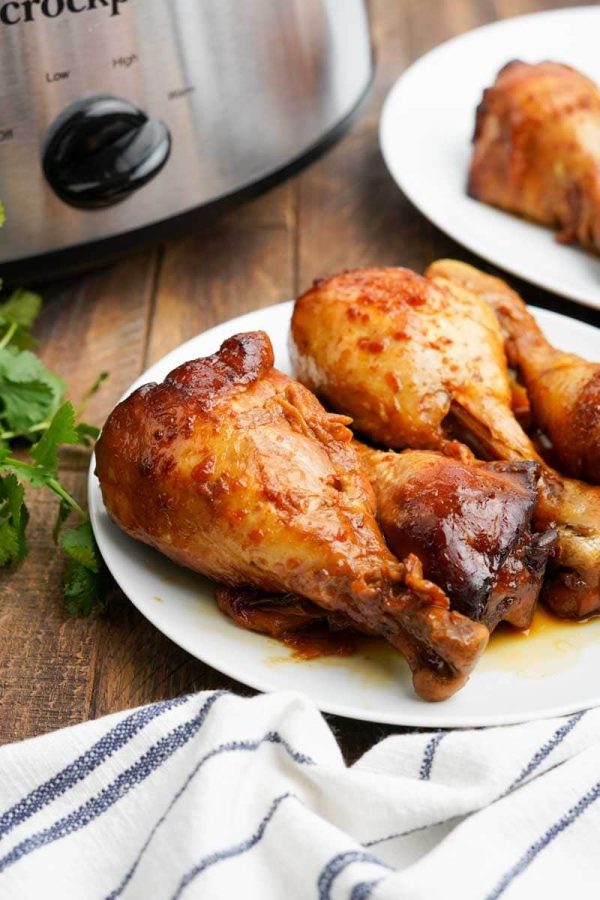 Crockpot chicken legs on a plate with a blue and white cloth napkin nearby.