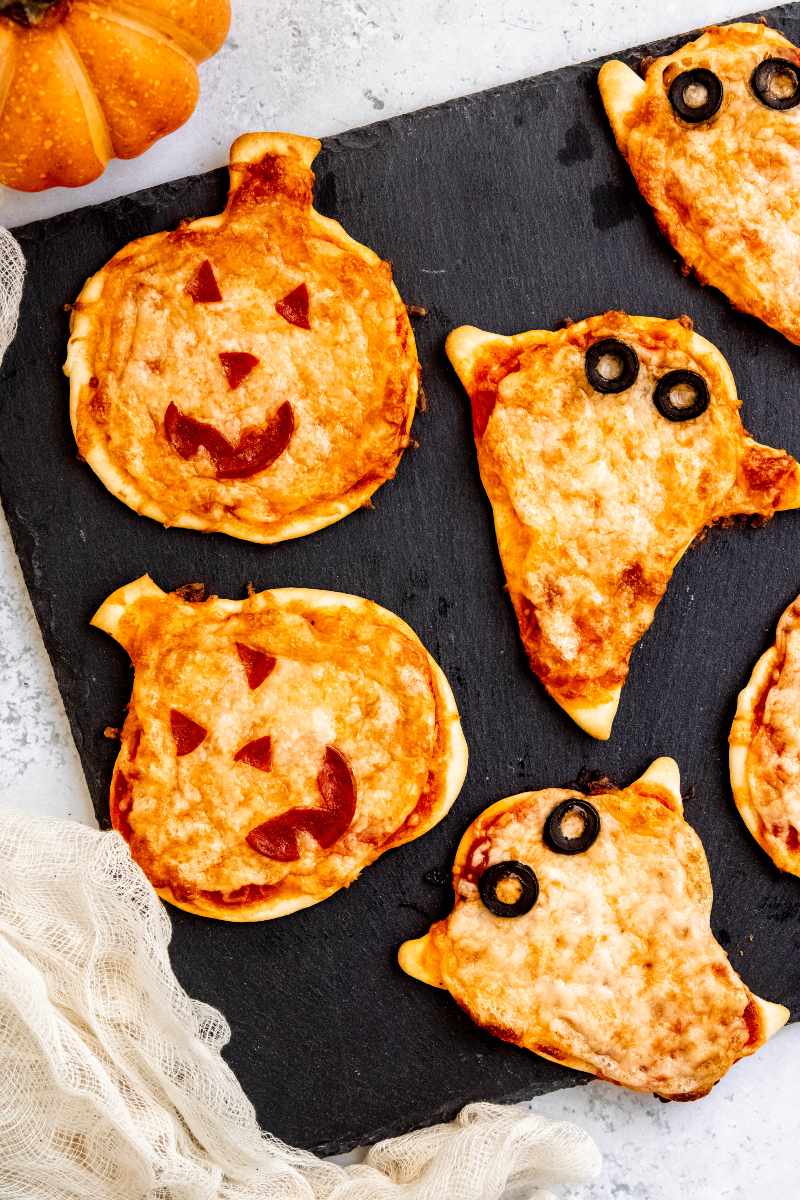 Mini halloween pizzas shaped like ghosts and jack-o-lanterns served up on a slate board.