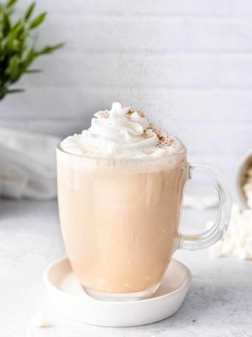 Cinnamon sprinkles down over the whipped cream garnish on a white chocolate mocha.