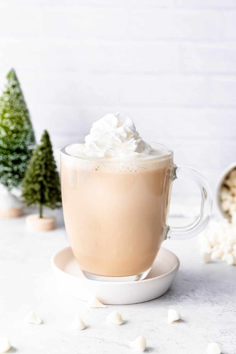 A holiday coffee drink stands on a white counter in front of decorative christmas trees.