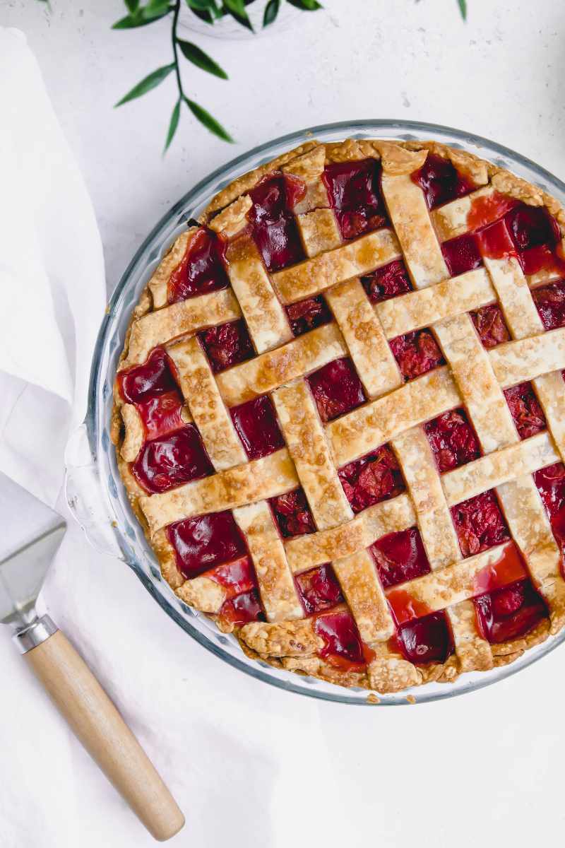A fully baked cherry pie with a lattice top cooled and ready to serve with a pie server nearby.