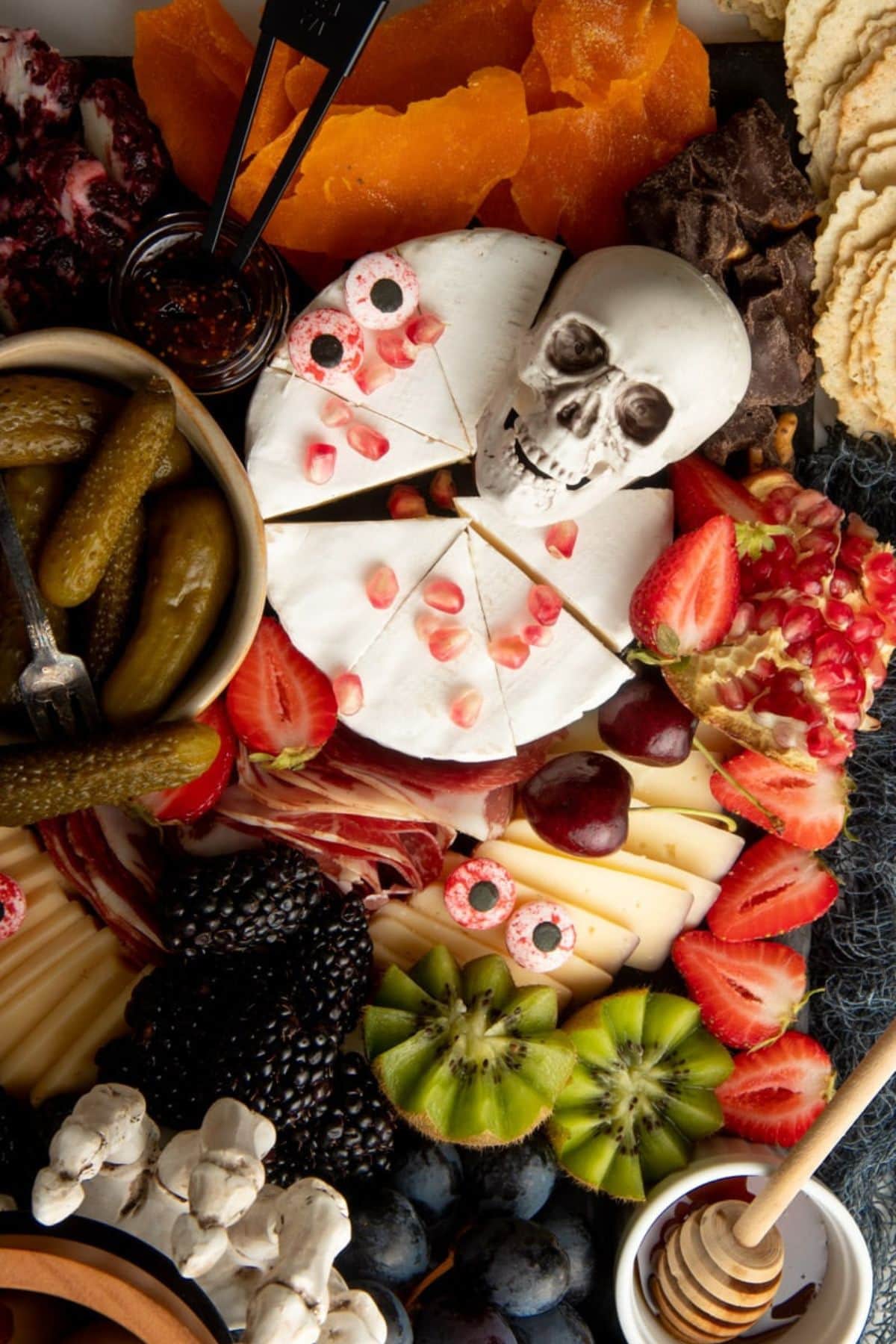 A plastic skull sits on top of a wheel of brie on a Halloween cheese board.