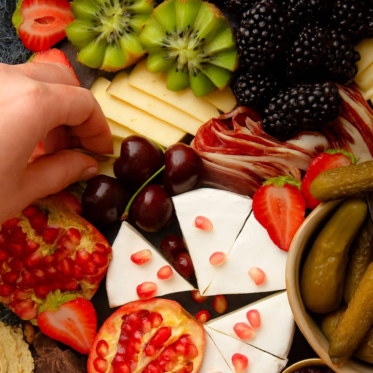 A hand adds cherries to a cheese board.