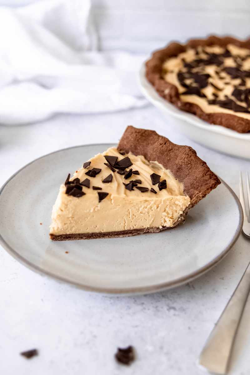 A slice of peanut butter pie with a chocolate crust rests on a ceramic plate with a fork beside it.