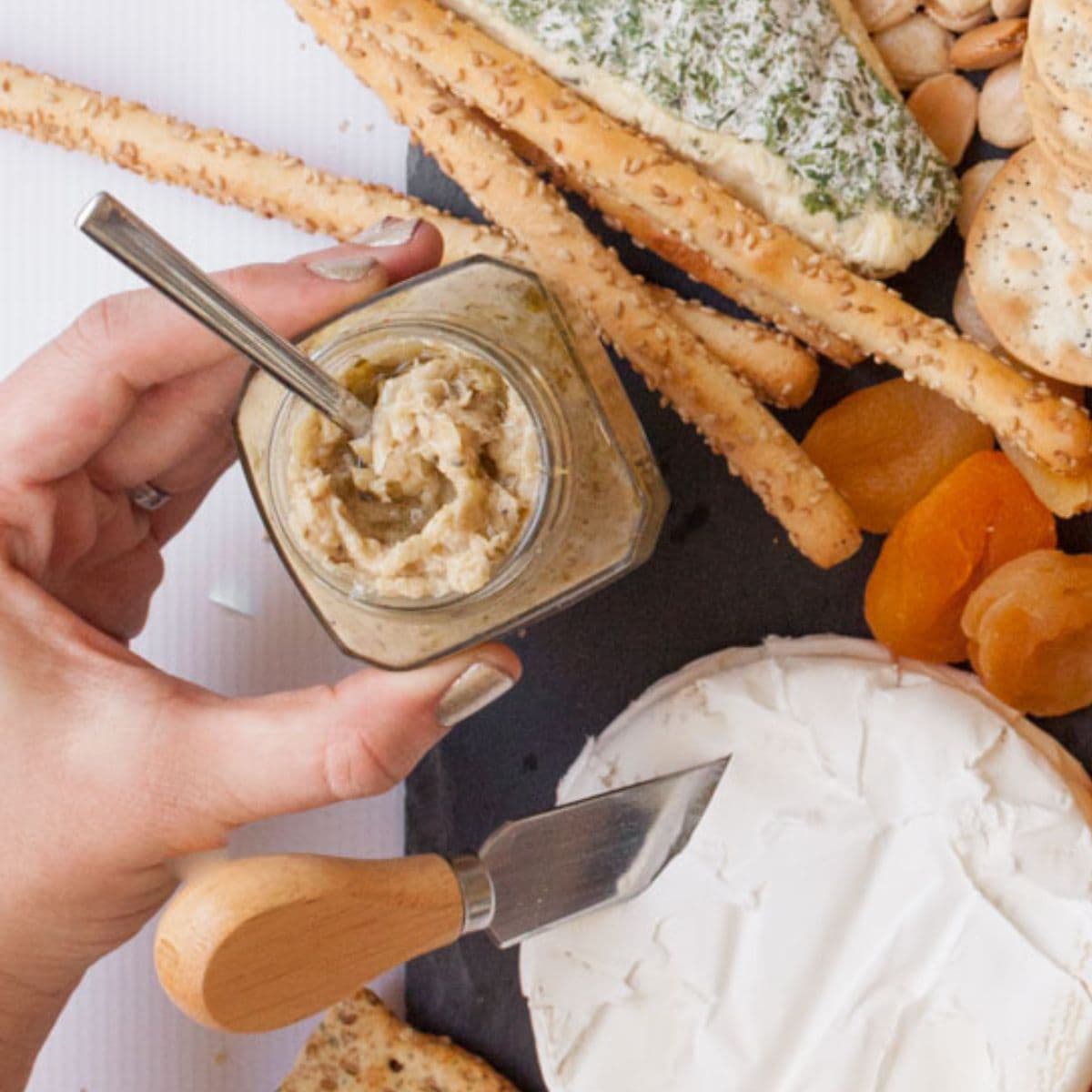 A hand places a small jar of chutney on a cheese board.