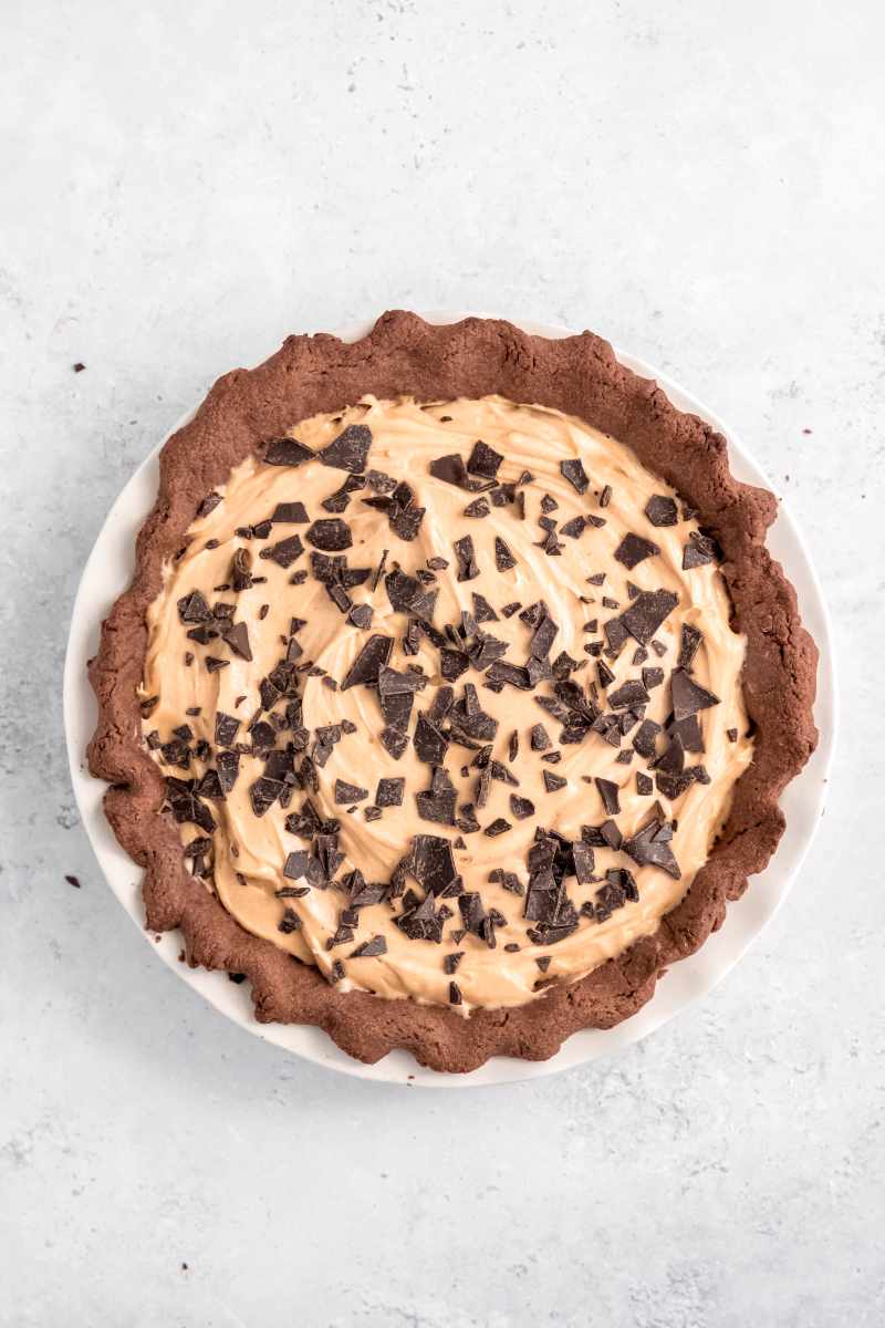 Overhead of a whole pie garnished with broken chocolate pieces in a white pie plate on a light counter.