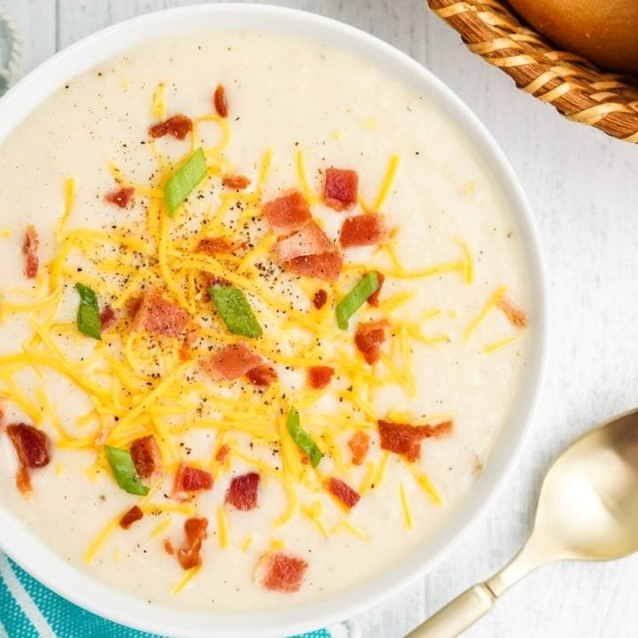 Overhead of a bowl of loaded potato soup with bread and shredded cheese nearby.
