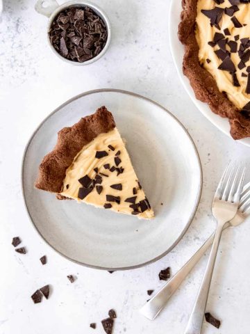 Overhead of a slice of peanut butter pie garnished with chocolate pieces on a ceramic plate with two forks nearby.