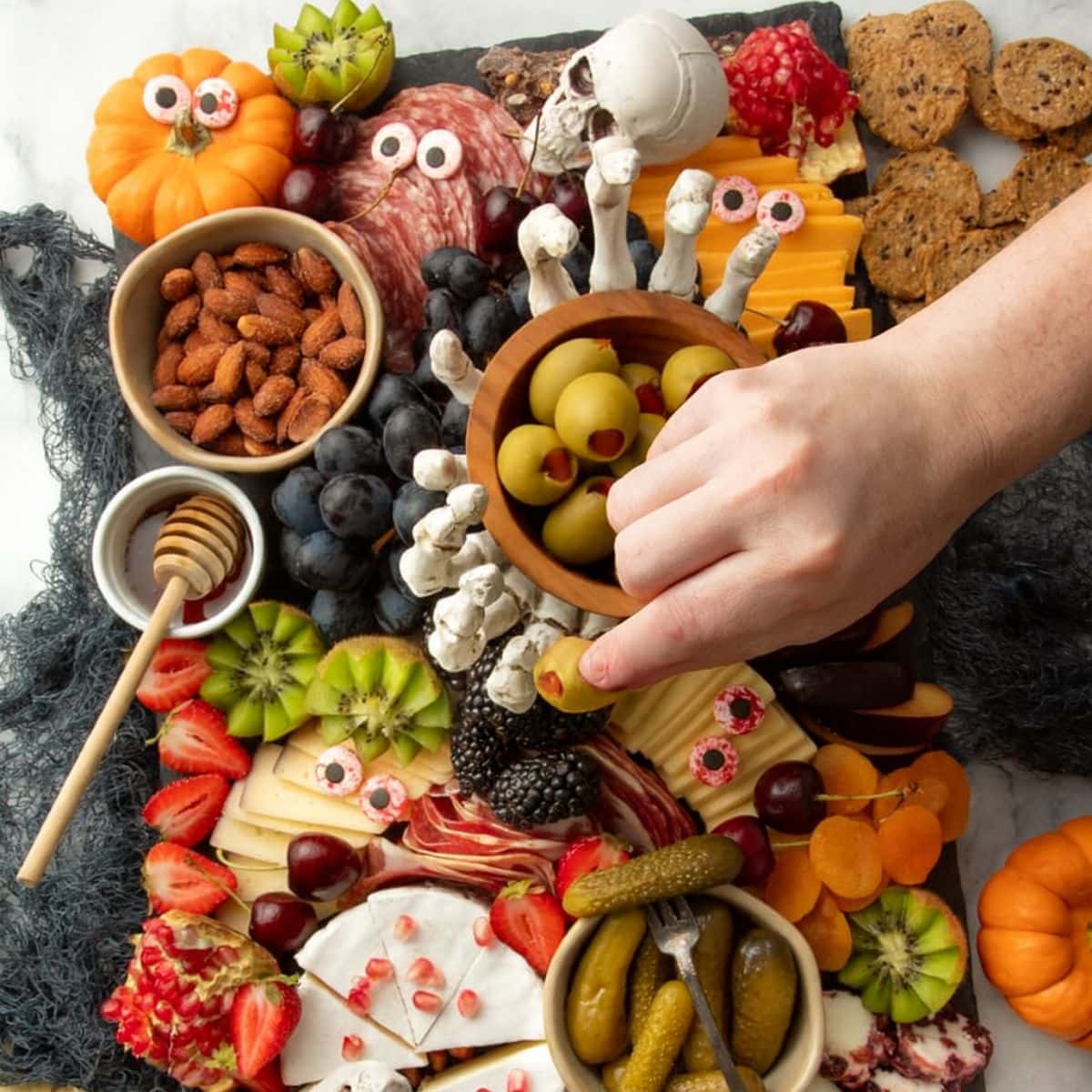 A hand reaches for an olive off of a Halloween charcuterie board