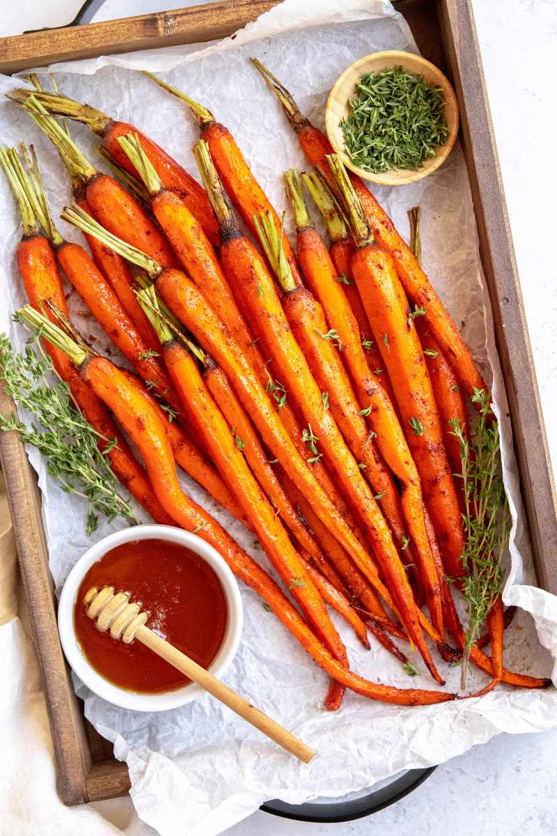 Overhead of simple glazed carrots served on a parchment paper lined tray with fresh thyme and honey.