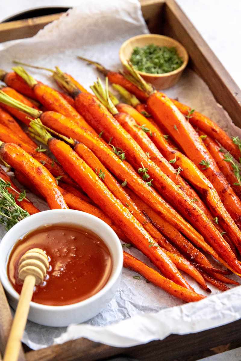Whole roasted carrots served on a wooden platter with fresh thyme and honey.