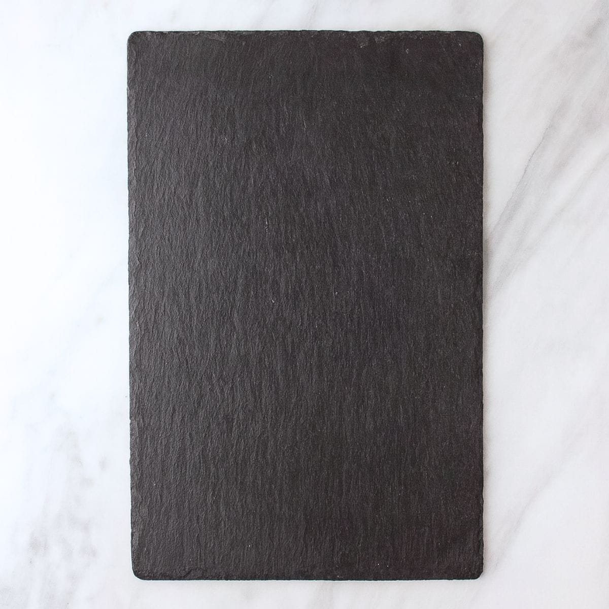 A black slate cheese board sits on a white marble countertop.
