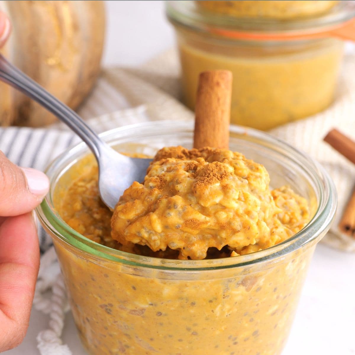 Spooning out a bite of pumpkin overnight oats from a clear glass jar