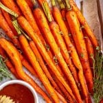 Honey glazed carrots served on a wooden tray with small bowls of honey and fresh thyme on either side.