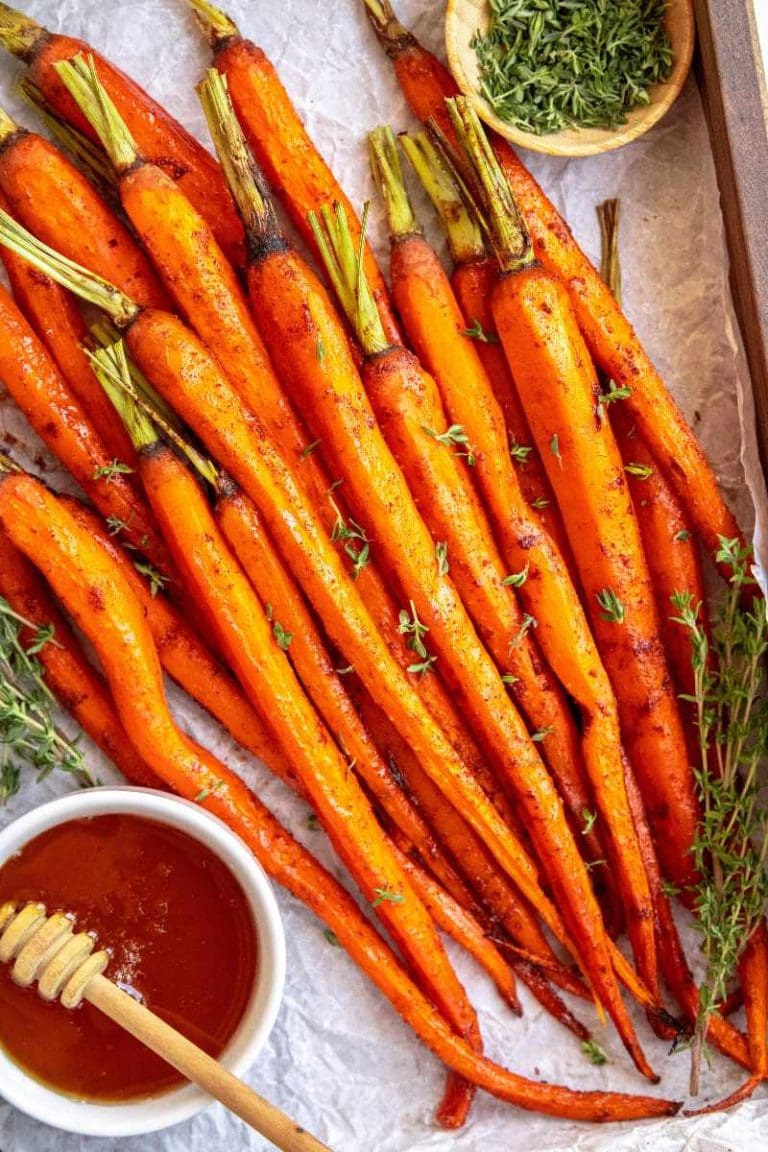 Honey glazed carrots served on a wooden tray with small bowls of honey and fresh thyme on either side.